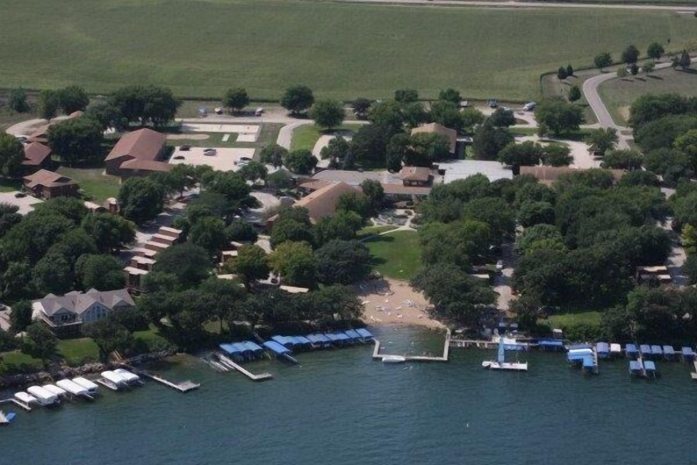 An aerial view of a lakeside property with multiple buildings, a dock with boats, and a beach area.