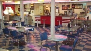 Een eetcafé met geruit vloerbedekking, blauwe stoelen en een balie met verschillende artikelen.