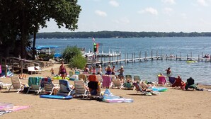 Een strand met ligbedden en parasols, een steiger en een helder uitzicht op het water.
