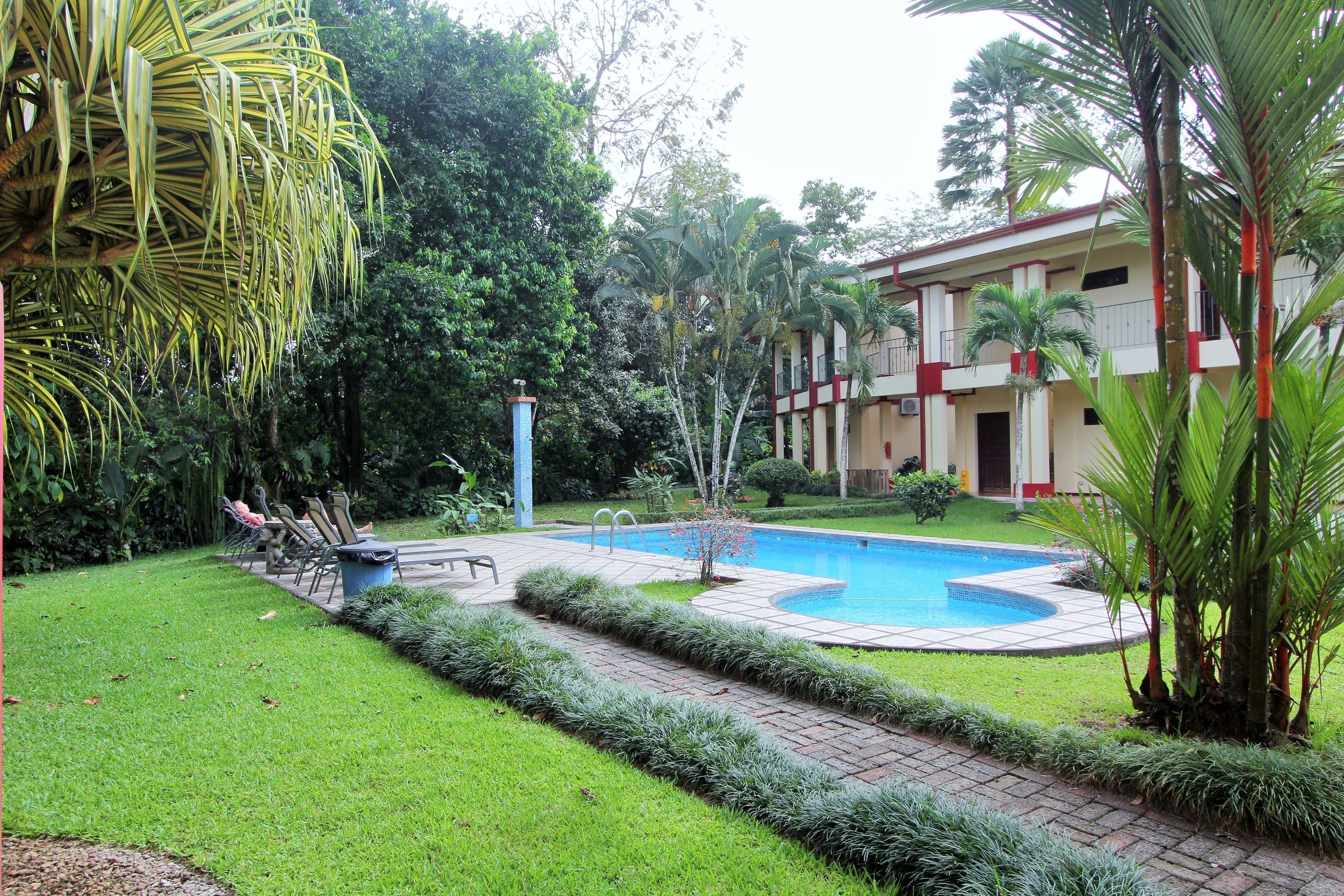 A swimming pool surrounded by a well-maintained lawn and a building with a red and white facade.