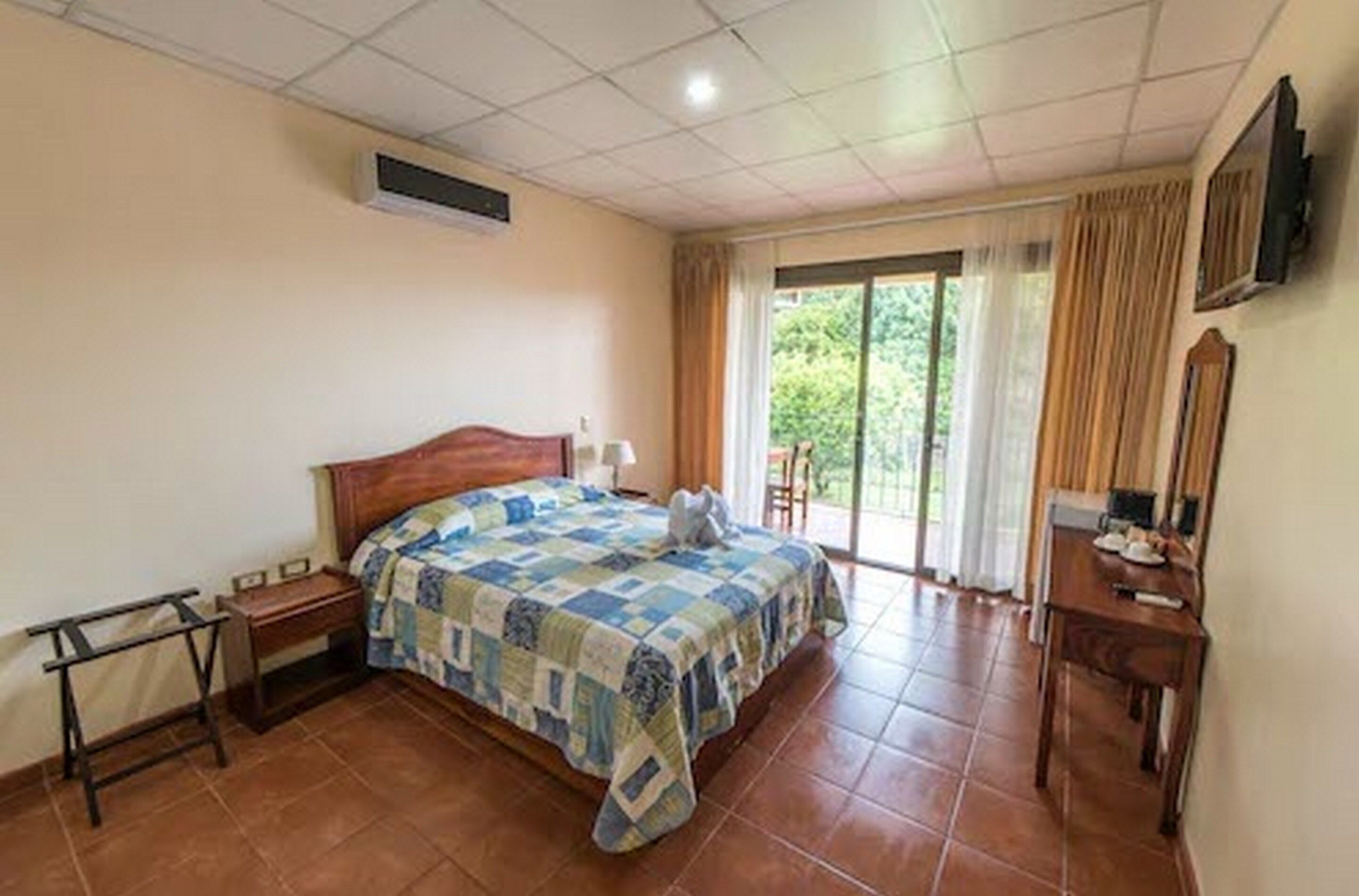 A bedroom with a bed, a desk, a chair, and a window with curtains.