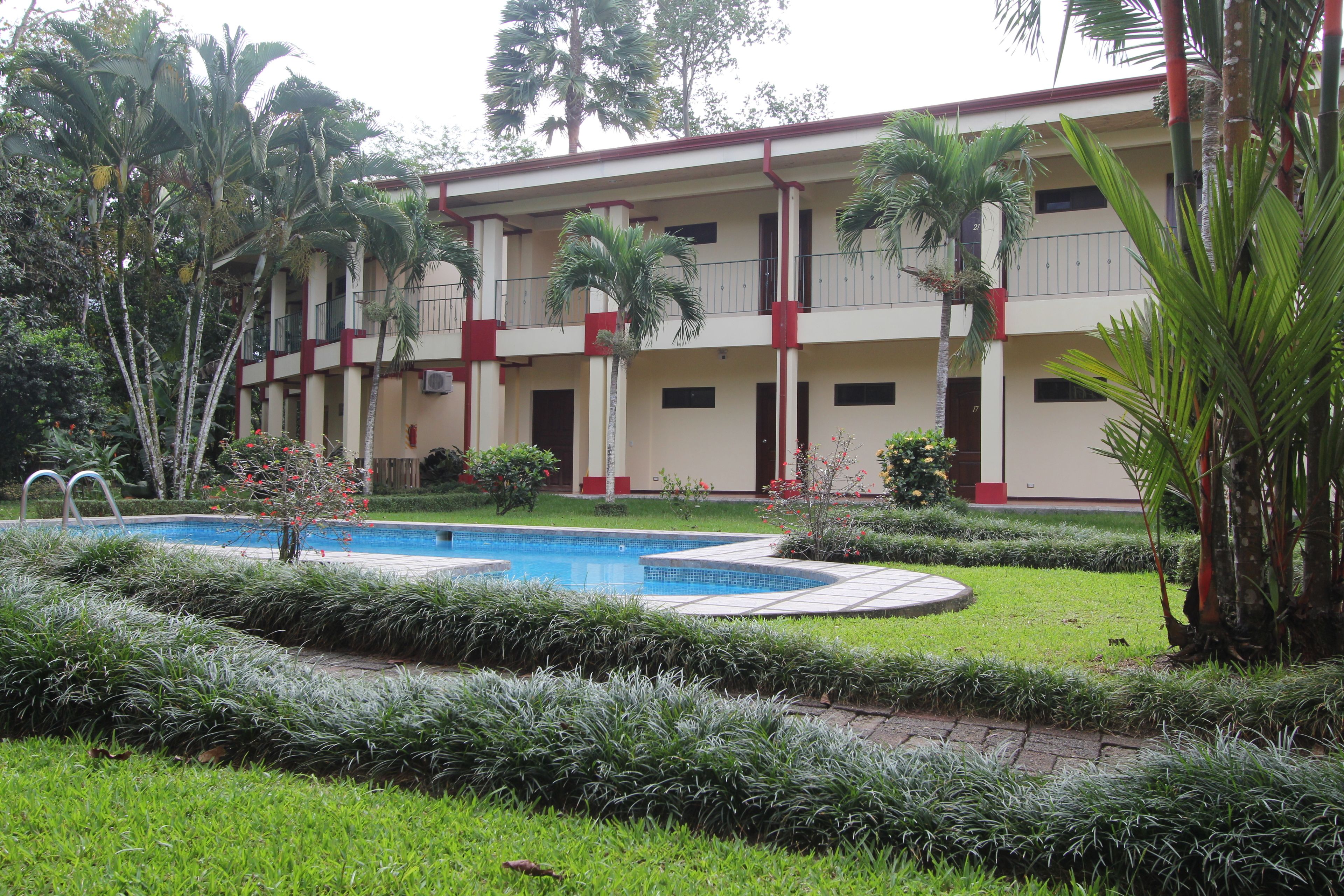 A hotel with a swimming pool, surrounded by well-maintained gardens and palm trees.