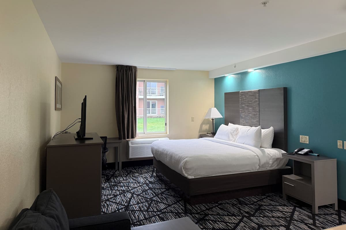 A hotel room with a bed, a desk, a chair, a lamp, and a phone on a bedside table.