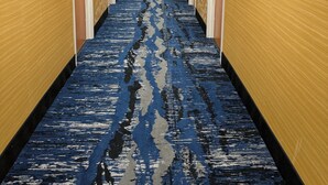 A hotel corridor with a patterned carpet, wooden walls, and doors on both sides. - Plymouth Bay Inn and Suites (Kingston)