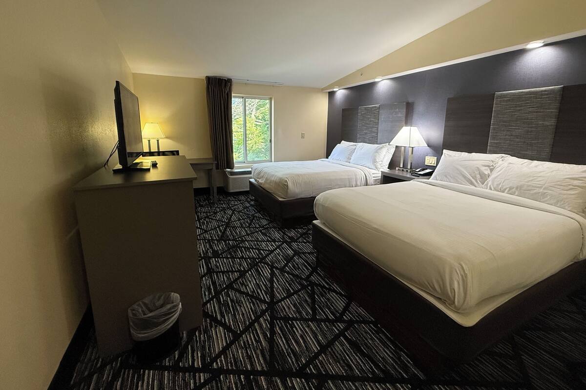 A hotel room with two beds, a desk, a chair, a waste bin, and a window with curtains.