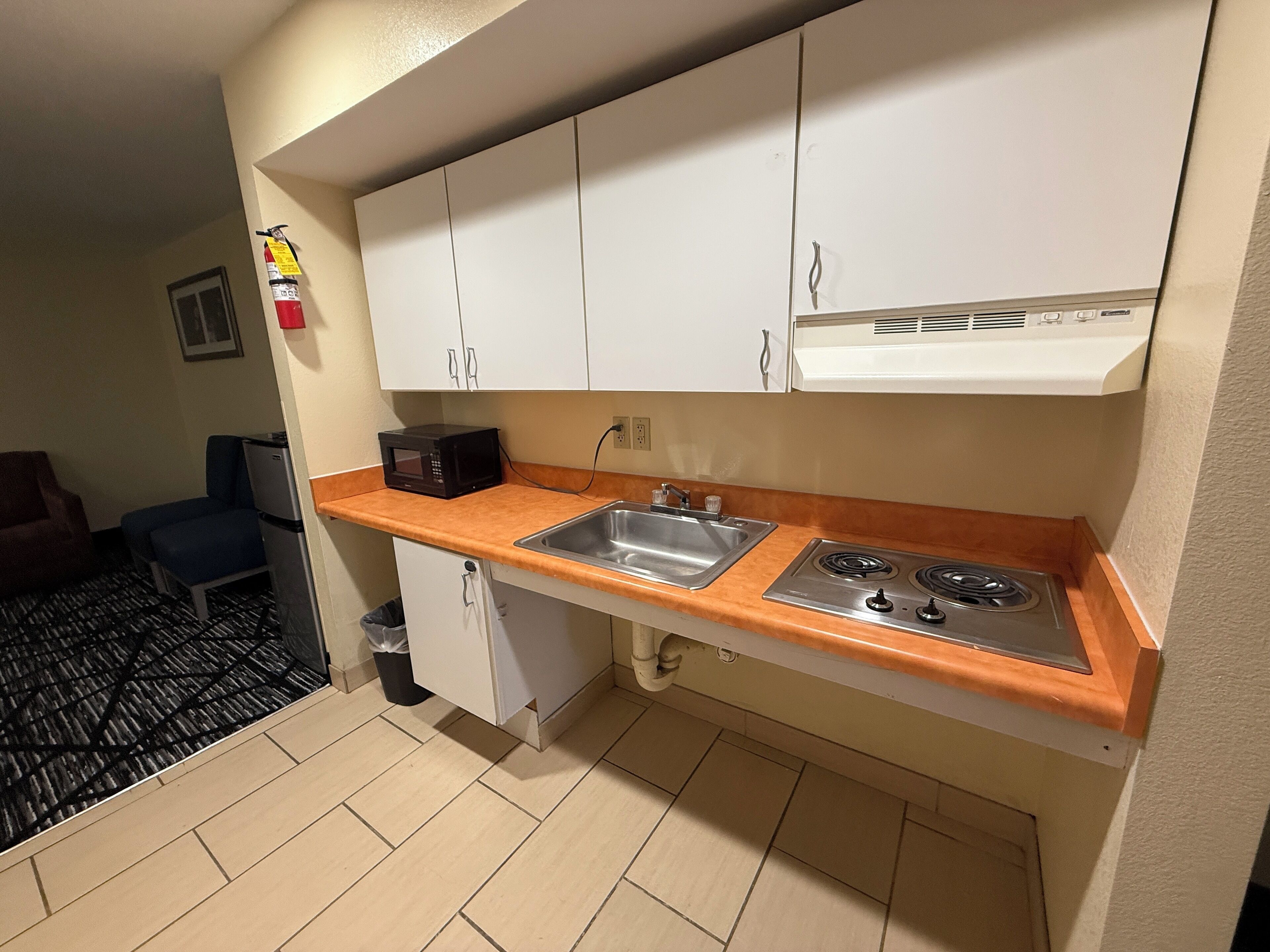 A compact kitchenette with white cabinets, a stainless steel sink, and a gas stove.