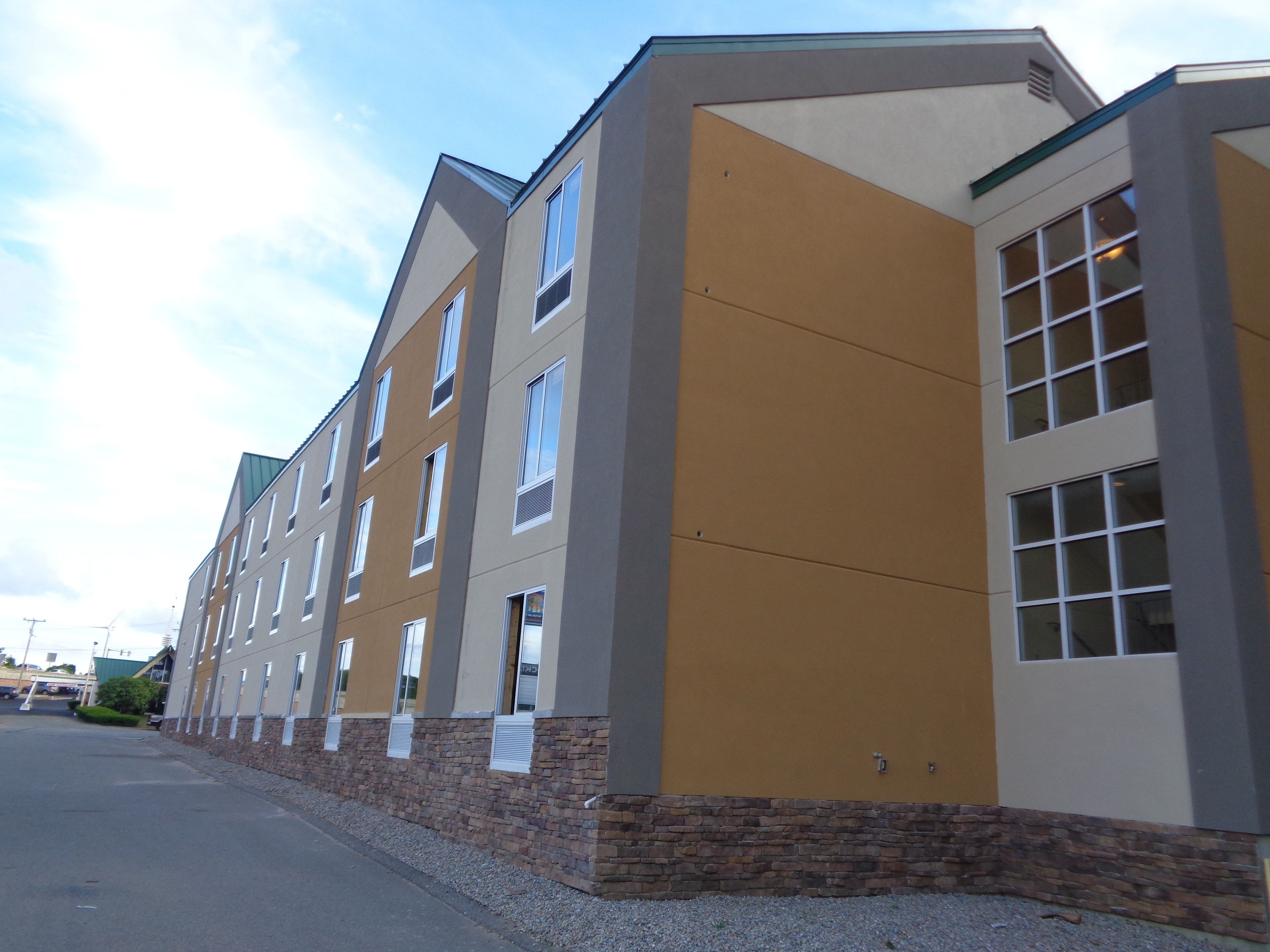 A multi-story hotel with a modern architectural design, featuring a combination of beige and brown exterior walls, large windows, and a stone base.