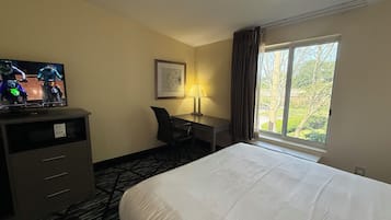 Hotellihuone, jossa on sänky, työpöytä, tuoli, televisio ja ikkuna, josta avautuu näkymä puita kohti.