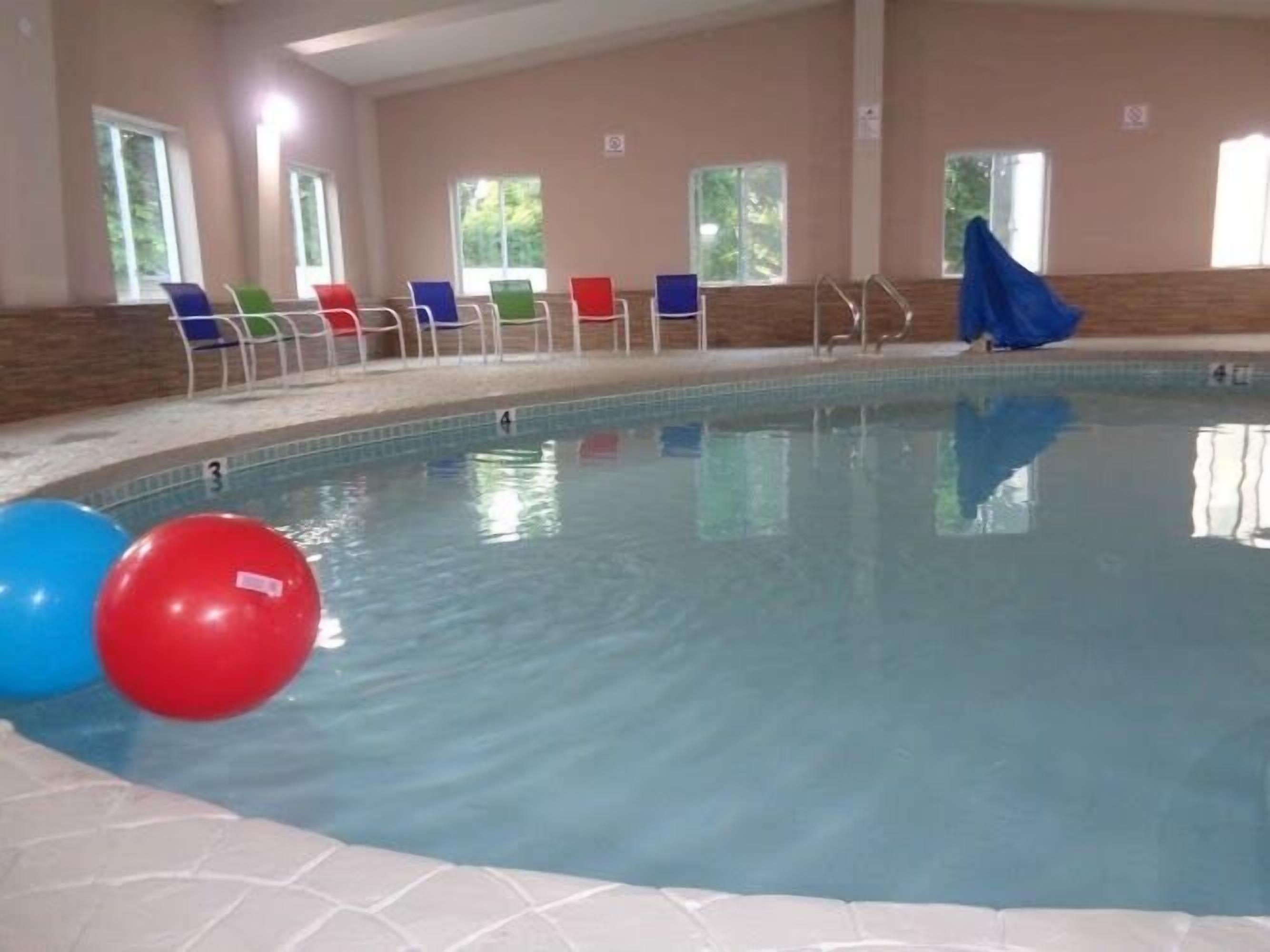 Una piscina interior con agua cristalina, rodeada de sillas y un suelo de baldosas.