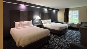 A hotel room with two beds, a desk, a lamp, and a window with a view of the outside. - Plymouth Bay Inn and Suites (Kingston)