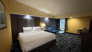 A hotel room with a large bed, a desk, a chair, a lamp, and a television.