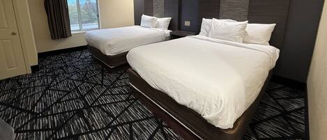 A hotel room with two beds, a window with curtains, a patterned carpet, and a dark wall with a light switch.