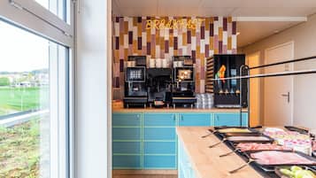 Ein Frühstücksbereich mit einer Theke, auf der verschiedene Speisen, eine Kaffeemaschine und eine Wand mit dem Schriftzug 'BREAKFAST' ausgestellt sind.