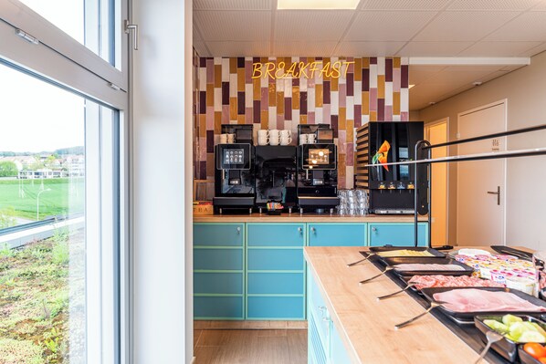 A breakfast area with a counter displaying various food items, a coffee machine, and a wall with a 'BREAKFAST' sign.