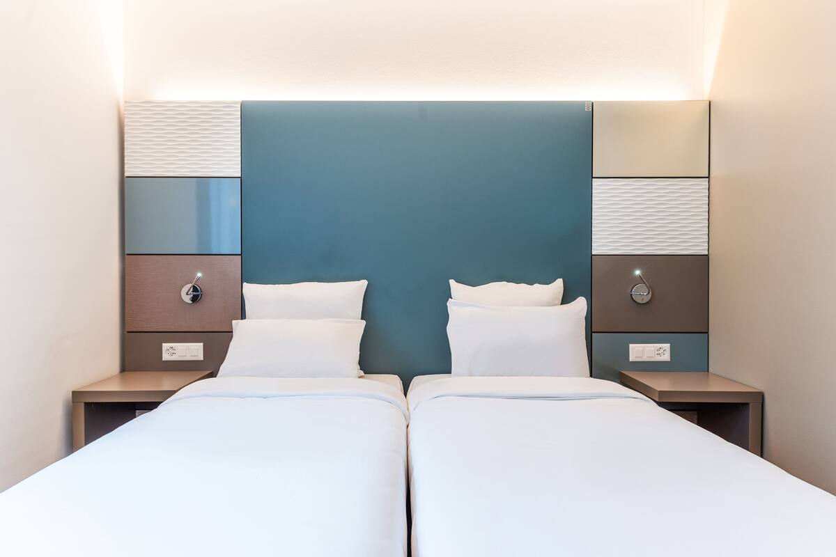 Un lit double avec une tête de lit, deux tables de chevet et un luminaire fixé au mur.