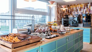 Een ontbijtbuffet met diverse gerechten, een koffiehoek en uitzicht op de stad door grote ramen.