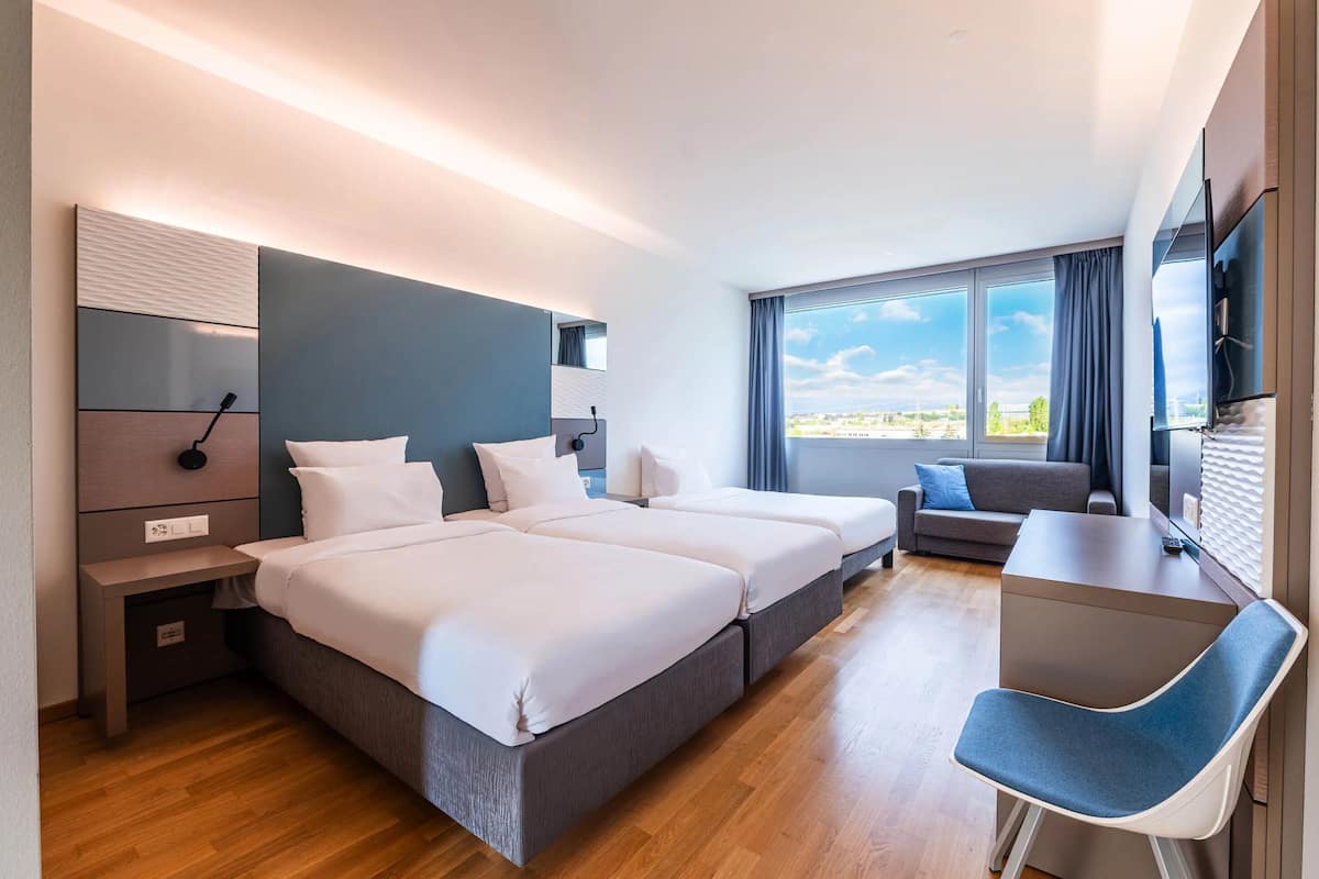 Une chambre d’hôtel moderne avec deux lits, un bureau et une vue sur la ville.