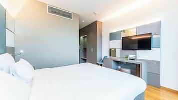 Una habitación de hotel moderna con una cama grande, un escritorio con televisión de pantalla plana y un armario.