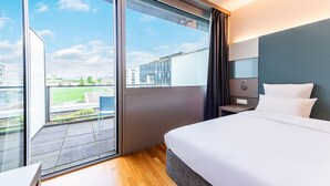 Een moderne hotelkamer met een groot balkon, een bed, een nachtkastje en uitzicht op de stad.