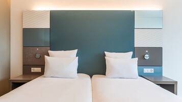 Een hotelkamer met twee bedden, een modern hoofdeinde, nachtkastjes met lampen en een wandlamp.