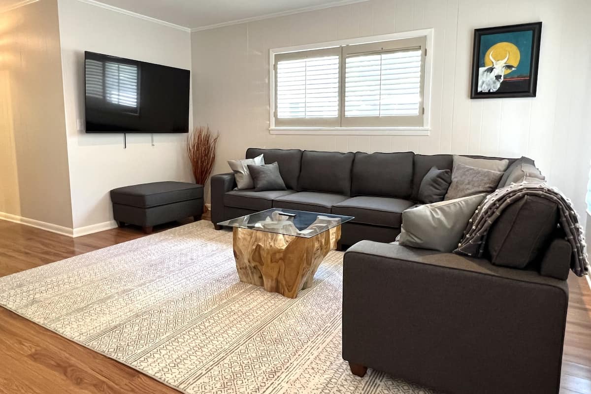 A modern living room with a sectional sofa, a coffee table, and a flat-screen TV mounted on the wall.