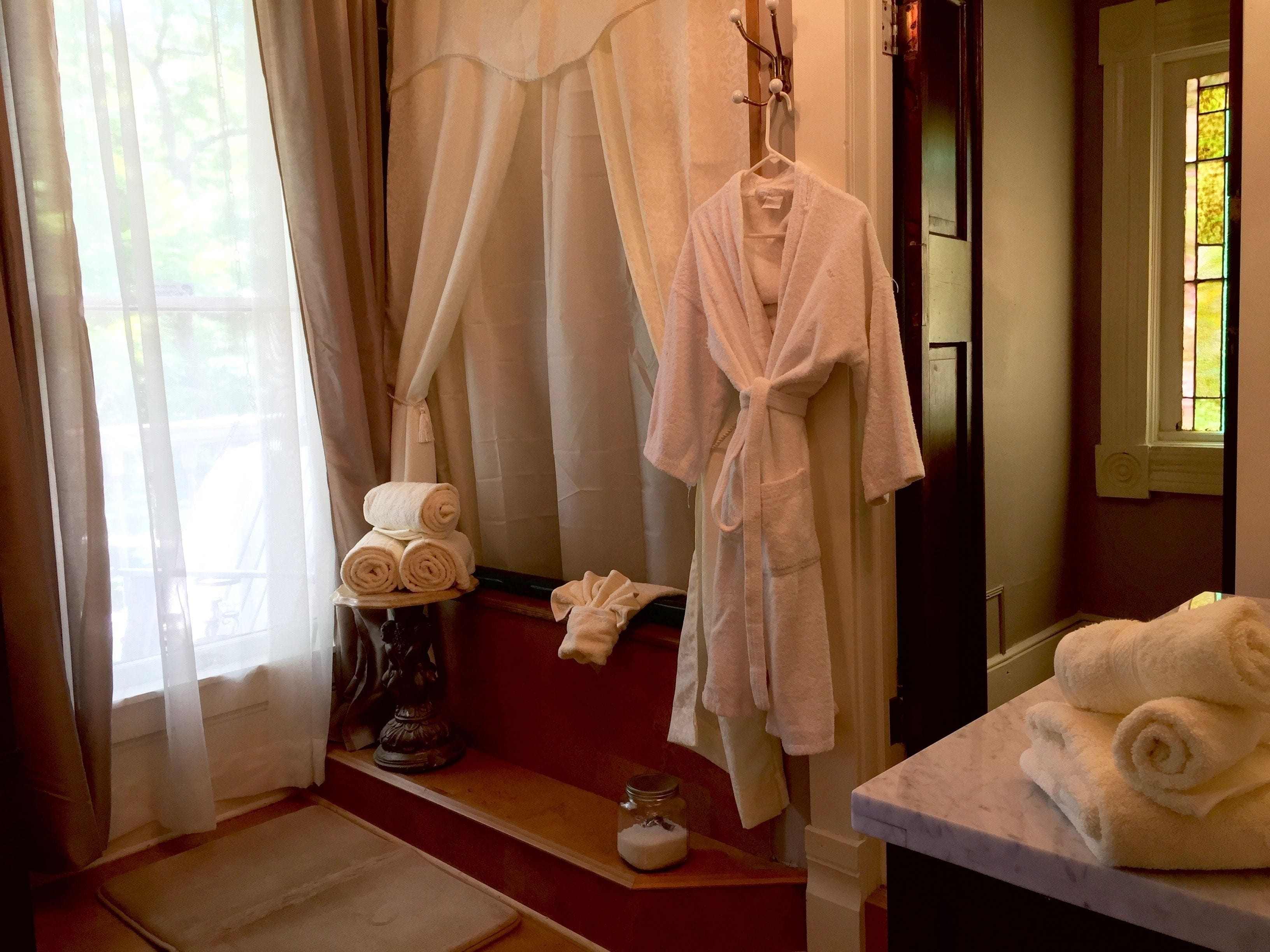 A bathroom with a bathtub, a robe hanging on a hook, and towels stacked on a shelf.