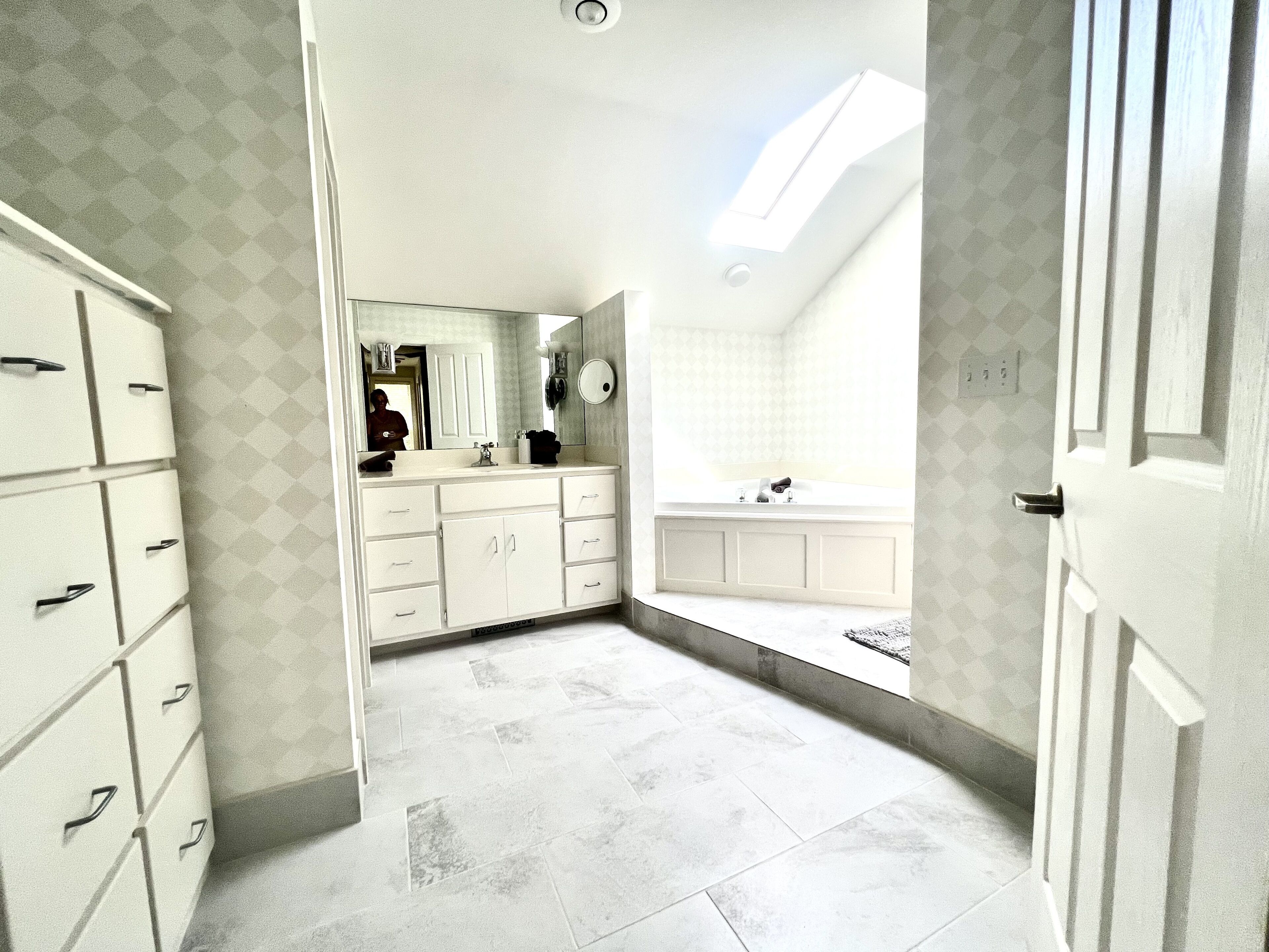 A bathroom with a large mirror, a bathtub, and a vanity with drawers.