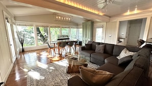A spacious living room with a large sofa, a coffee table, and a dining area with a wooden table and chairs. There is a ceiling fan and a large window providing natural light. - Eureka Zen Cottages (Eureka Springs)