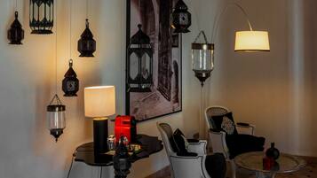 Een kamer met een ronde tafel, een stoel, een lamp, een rood voorwerp en meerdere wandlampen.