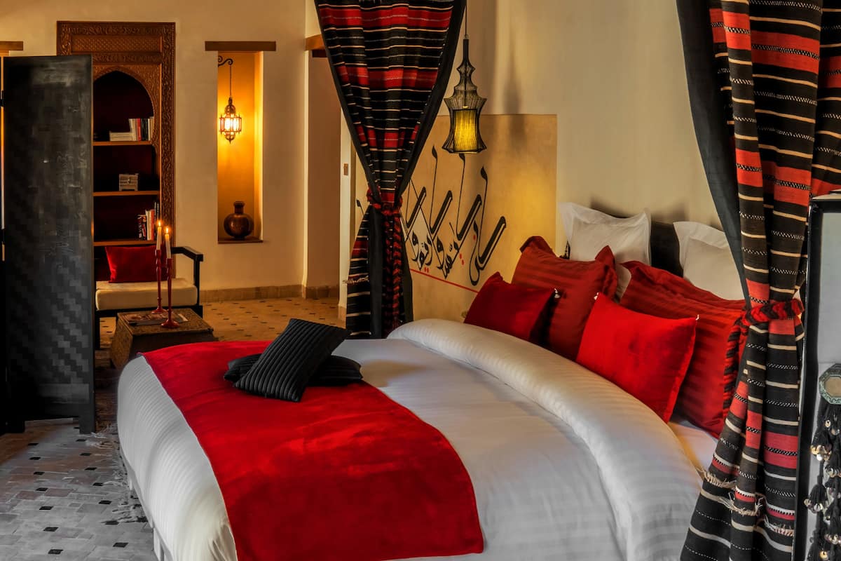 Ein Hotelzimmer mit einem großen Bett, rot-weiß gestreifter Bettwäsche, einem Bücherregal und einer Wand mit Kalligrafie.