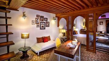 A cozy room with a wooden ceiling, a sofa with patterned cushions, a small table with a lamp, and a wall adorned with framed pictures.