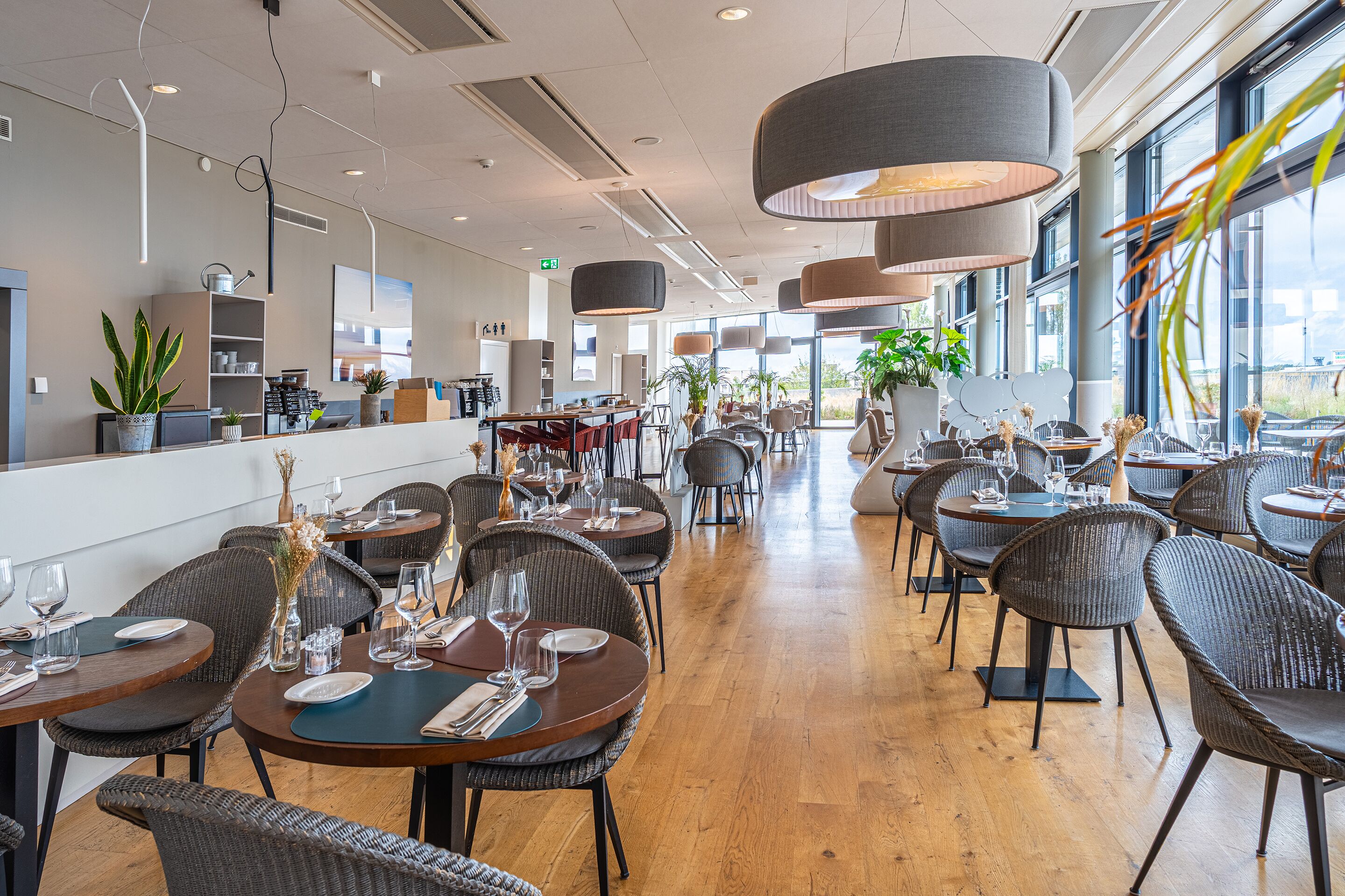 A modern restaurant with round tables, wicker chairs, and pendant lighting.