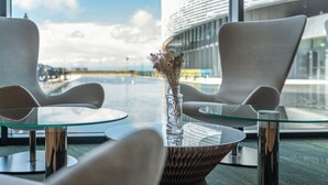 A modern interior with two glass-top tables, a vase with dried flowers, and a view of a building through large windows. - Aquatis Hotel (Lausanne)