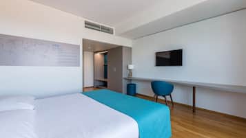 Ein modernes Hotelzimmer mit Bett, Schreibtisch, Stuhl, Fernseher und einer Weltkarte an der Wand.