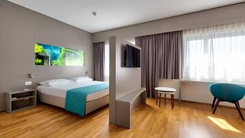 Una camera d'albergo moderna con un letto, una scrivania, una sedia e un'ampia finestra con tende.