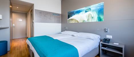 A modern hotel room with a bed, a desk, and a wall-mounted TV displaying a nature scene.