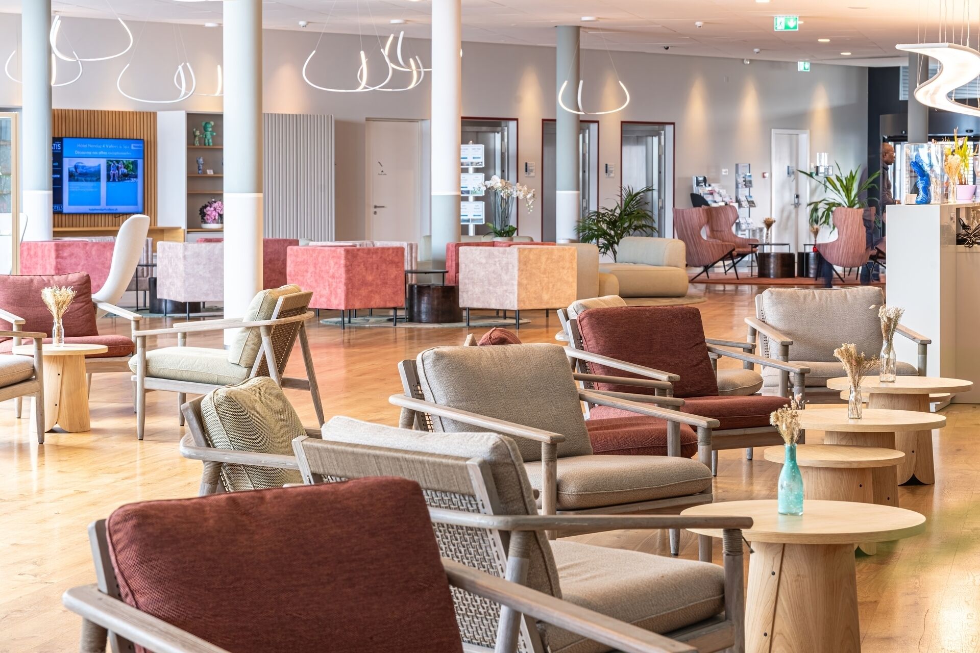 Eine moderne Hotelhalle mit mehreren Sitzbereichen, darunter Sofas und Sessel, die um einen zentralen Couchtisch angeordnet sind.