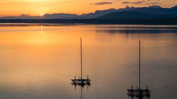 A calm lake with two sailboats anchored, mountains in the background, and a sunset.