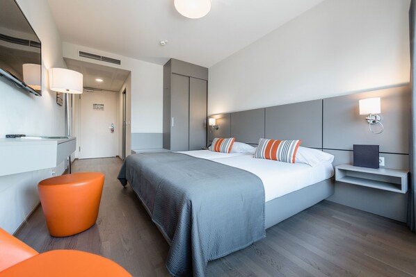 Una habitación de hotel moderna con una cama grande, una mesita de noche, una silla y un espejo.