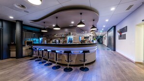A bar area with a curved counter, multiple stools, and overhead lighting. - Lake Geneva Hotel (Versoix)