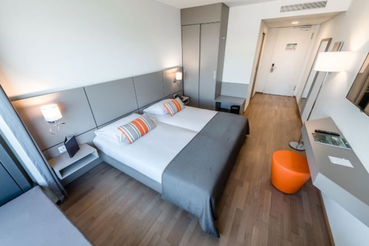 A hotel room with a bed, bedside tables, a desk, and a chair.