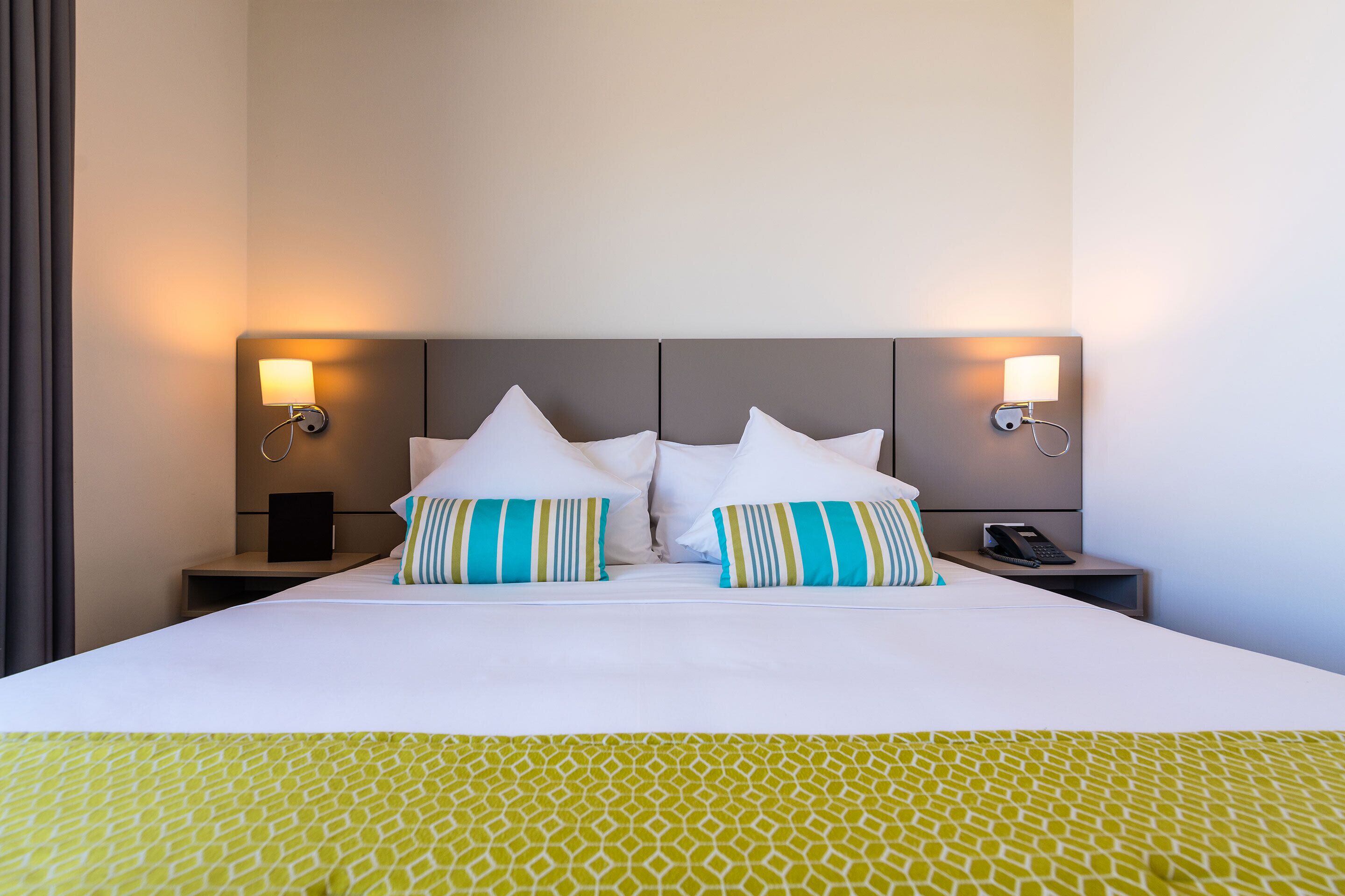 Habitación de hotel con una cama grande, dos lámparas de noche, un teléfono en la mesita de noche y una mesita de noche con lámpara.