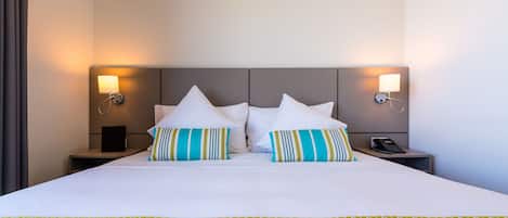 Habitación de hotel con una cama grande, dos lámparas de noche, un teléfono en la mesita de noche y una mesita de noche con lámpara.