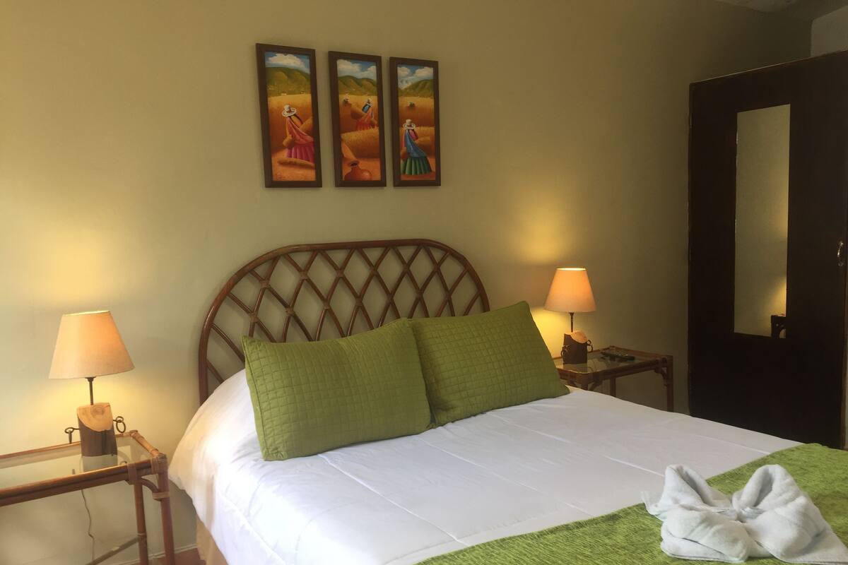 Una cama bien hecha con sábanas blancas, almohadas verdes, dos lámparas de noche y un cabecero de madera.