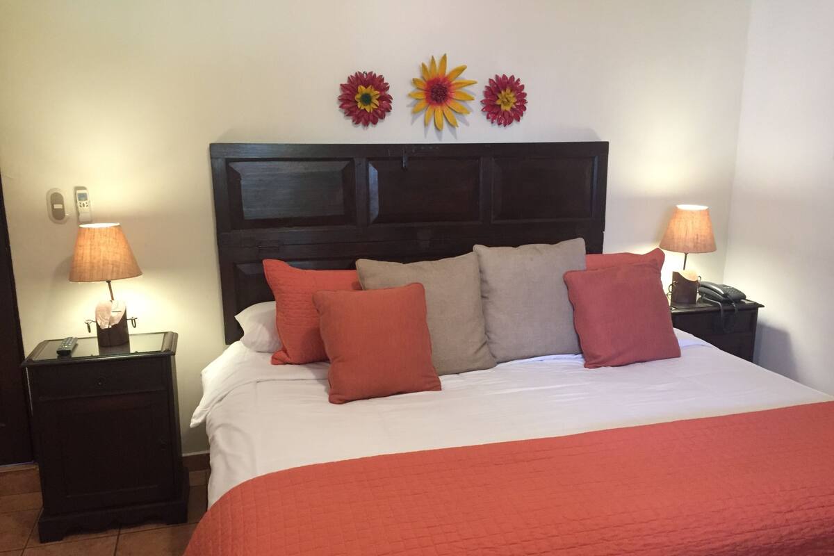 Una habitación de hotel con una cama grande, dos mesitas de noche y una lámpara de pared.