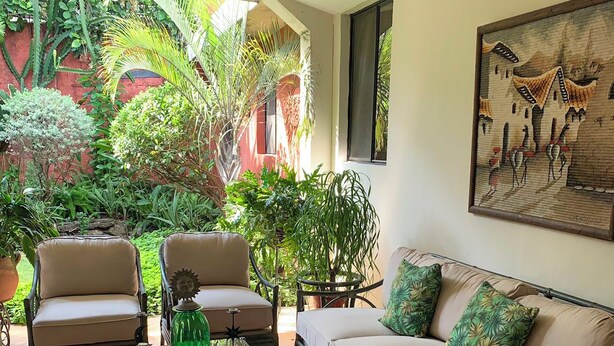 A cozy living room with a sofa, two armchairs, and a coffee table. There is a large window with a view of a garden. - Hotel La Posada del Angel (San Salvador)