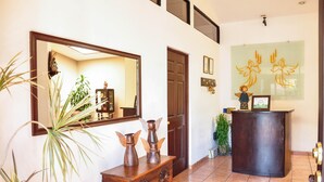 A reception area with a wooden desk, a large mirror, and a wall-mounted artwork. - Hotel La Posada del Angel (San Salvador)