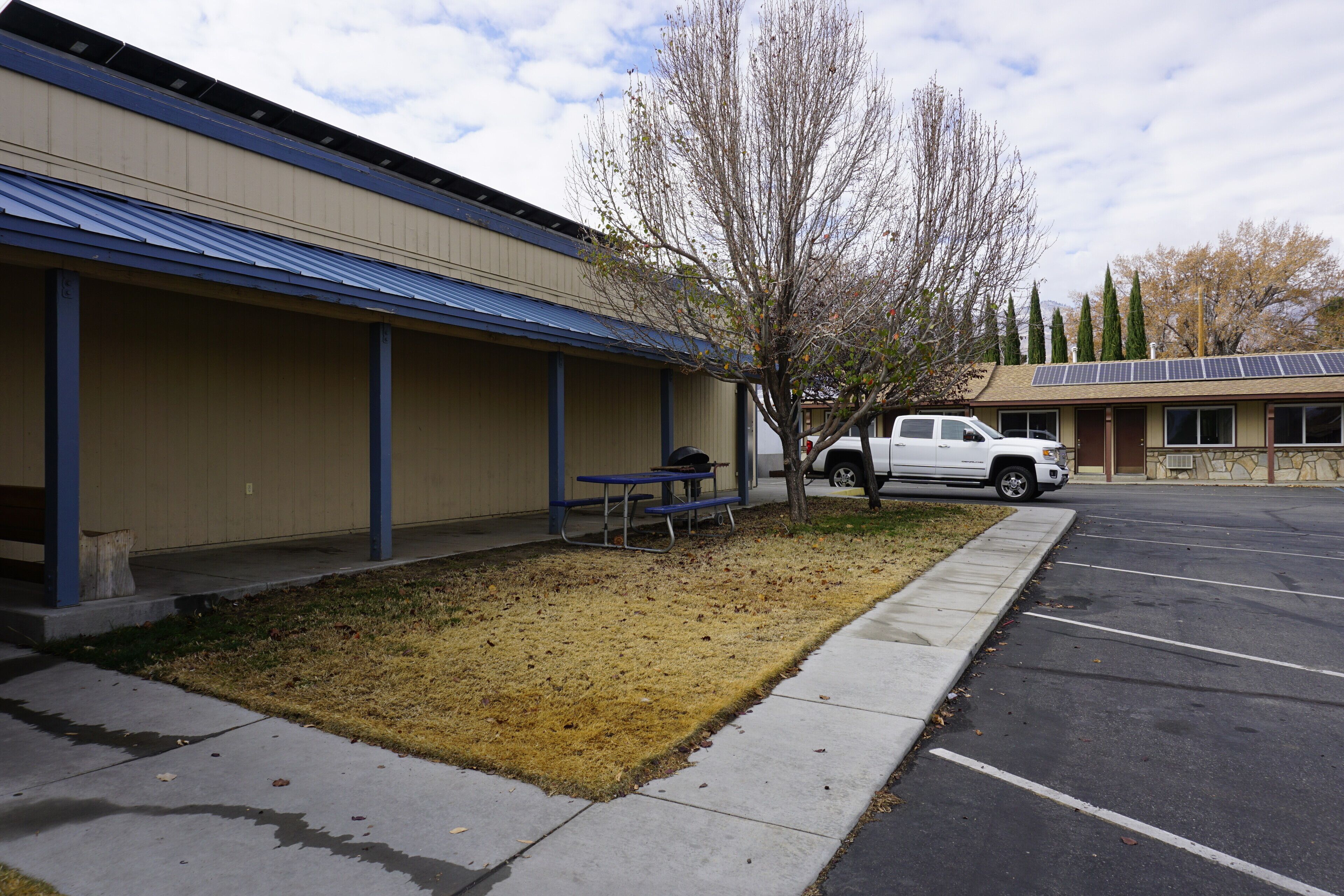 A building with a covered outdoor seating area, a parking lot, and a tree.