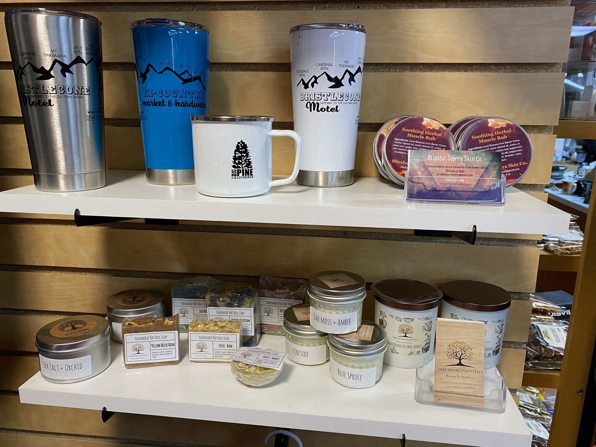 A shelf with various products including mugs, candles, and jars of natural soaps.