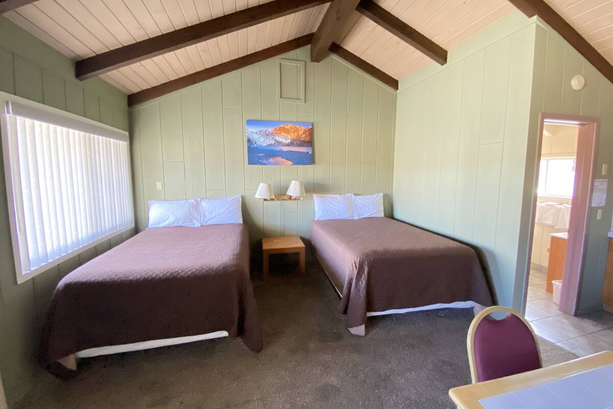 A room with two beds, a small table, and a painting on the wall.